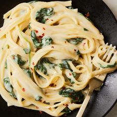 a black bowl filled with pasta and spinach