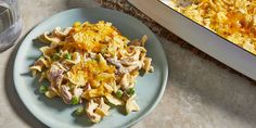 a blue plate topped with pasta next to a casserole dish filled with chicken and vegetables