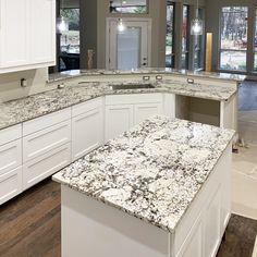 an empty kitchen with white cabinets and granite counter tops in front of two large windows