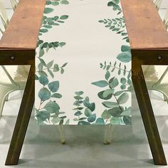 the table is set with two white chairs and a long wooden table that has green leaves on it