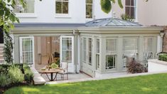 an orangery in the middle of a garden with tables and chairs