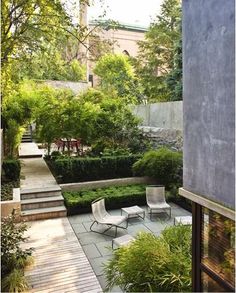 an outdoor patio with chairs and plants in the center, surrounded by greenery on both sides