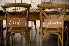 two wooden chairs with bride and groom signs on their backs sitting at a dining room table