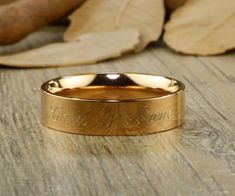 a close up of a gold wedding ring on a wooden surface with leaves in the background