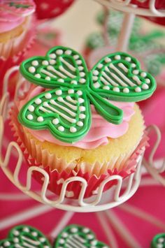 cupcakes decorated with green and pink icing are on a cake stand in front of other cupcakes