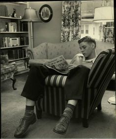 a young man sitting in a chair reading a magazine while wearing boots and socks on his feet