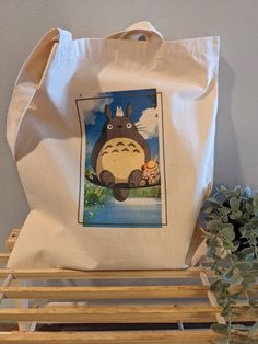 a tote bag sitting on top of a wooden bench next to a plant and potted plant