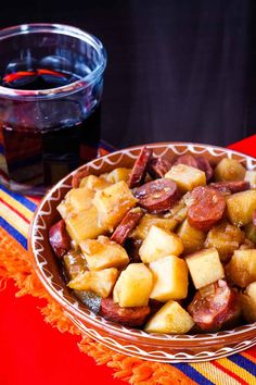 a bowl filled with potatoes and sausage next to a glass of wine