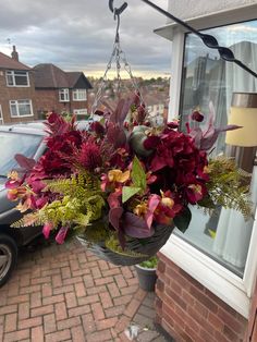 a hanging basket filled with lots of flowers next to a car parked in front of a building