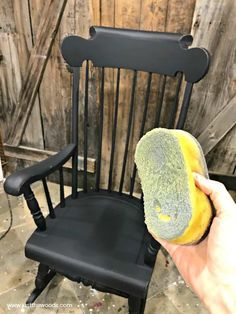 a person holding a sponge in front of a black rocking chair with wood slats