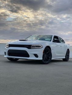 a white dodge charger parked in a parking lot next to the ocean and cloudy sky