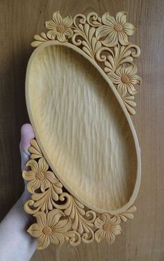 a hand is holding a wooden tray with flowers on the bottom and an intricately carved design