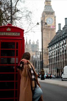 a woman leaning against a red phone booth on the street with big ben in the background