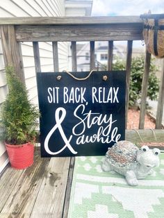 a sign that says sit back relax and stay awhile on a porch next to a potted plant