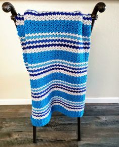 a blue and white crocheted blanket sitting on top of a wooden chair next to a wall