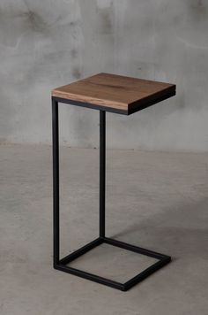 a square wooden table with metal legs on concrete floor next to grey wall and cement background