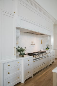 a kitchen with white cabinets and gold pulls on the doors, an oven in the center