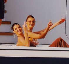 two women are sitting on the back of a boat and waving at the camera man