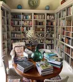 a room filled with lots of books next to a table covered in flowers and vases