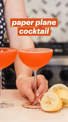 two wine glasses with orange juice and lemon wedges on a counter top next to a woman's hand