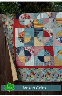 a quilted blanket with circles and flowers on it, sitting next to a fence