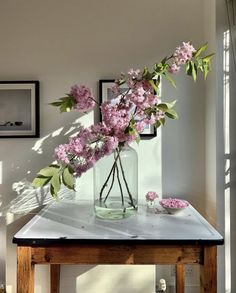 a vase with pink flowers on a table in front of some framed pictures and windows