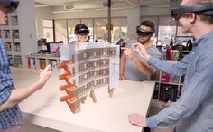 three men wearing virtual headsets stand around a model of a building in a library