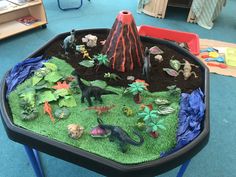 a play area with toys and plants in the shape of a volcano on top of green grass