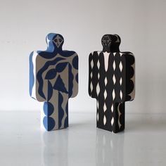 two wooden sculptures sitting side by side on a white surface, one is black and the other is blue