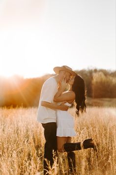 a man and woman are kissing in the middle of a field with tall grass at sunset