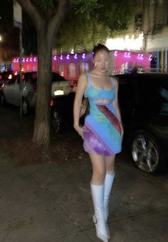 a woman in a short dress and knee high boots walking down the street at night