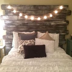 a bed with white sheets, pillows and lights on the headboard is made from wood planks