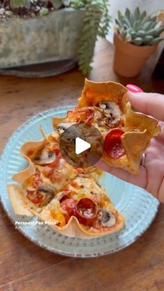 a person holding up a slice of pizza on top of a blue plate in front of a potted plant