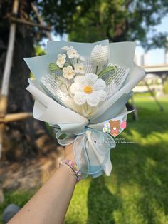 a person holding a bouquet of flowers in their hand with the grass and trees behind them