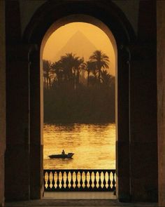 a person in a boat on the water near an arch with a view of mountains and palm trees