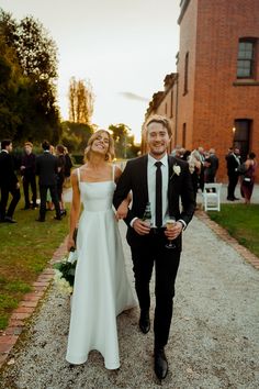 a man and woman in formal wear walking down a path with champagne glasses on their feet