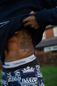 a man with tattoos on his stomach wearing blue shorts and a black sweater is standing in the grass