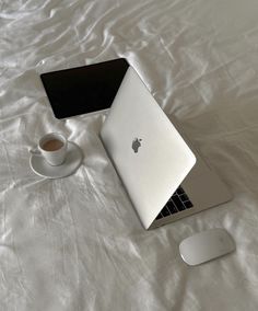 an apple laptop computer sitting on top of a bed next to a cup of coffee