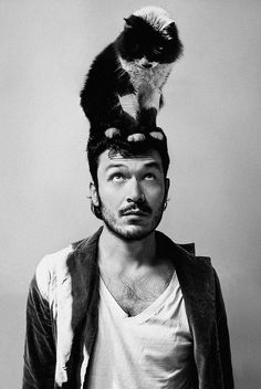 a black and white photo of a man with a cat on his head in front of him