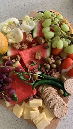 a variety of cheeses, fruits and vegetables on a cutting board with crackers