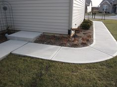 a concrete walkway in front of a house with grass and bushes on the ground next to it