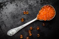 a spoon filled with red cavia pearls on top of a black surface next to some nuts