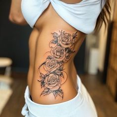 a woman's stomach with roses and leaves tattoo on her lower side ribcage