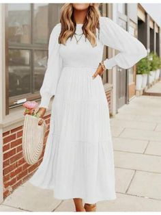 a woman wearing a white dress standing on the sidewalk with her hands in her pockets