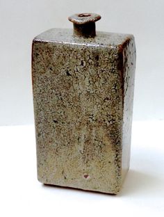 a square vase with a small hole in the middle on a white surface, it appears to be holding something