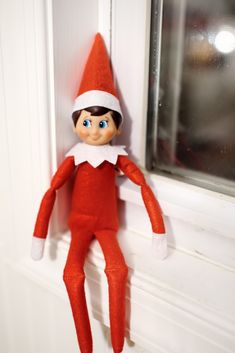 an elf doll hanging from the side of a window sill with its eyes open