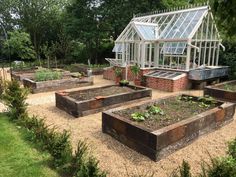 an outdoor garden area with raised beds and greenhouse in the background, surrounded by trees