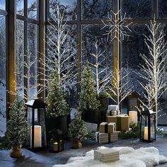 christmas trees and presents in front of large windows with snow outside at night, lit by candles