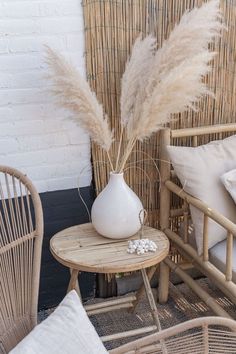 a white vase sitting on top of a wooden table next to a wicker chair