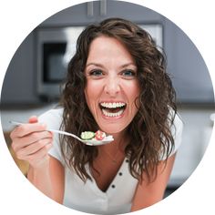 a woman is smiling while holding a spoon with food on it in front of her face